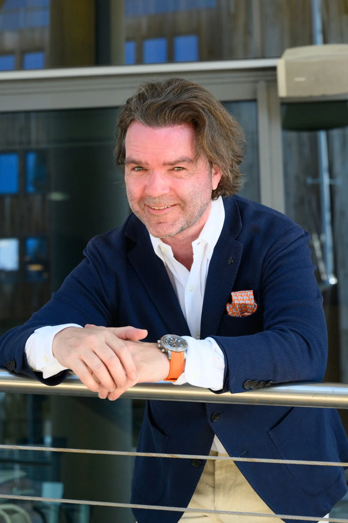 Finn-Robert Kristensen i mørkeblå blazer og hvit skjorte, lent mot et rekkverk utendørs, med et rolig smil mot kamera.